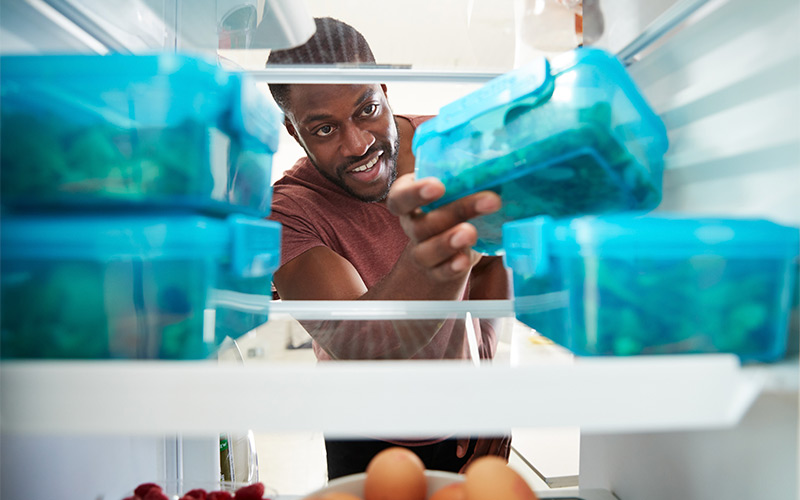 Front view of man reaching inside the refrigerator for meal prep containers. Front view of man reaching inside the refrigerator for meal prep containers.